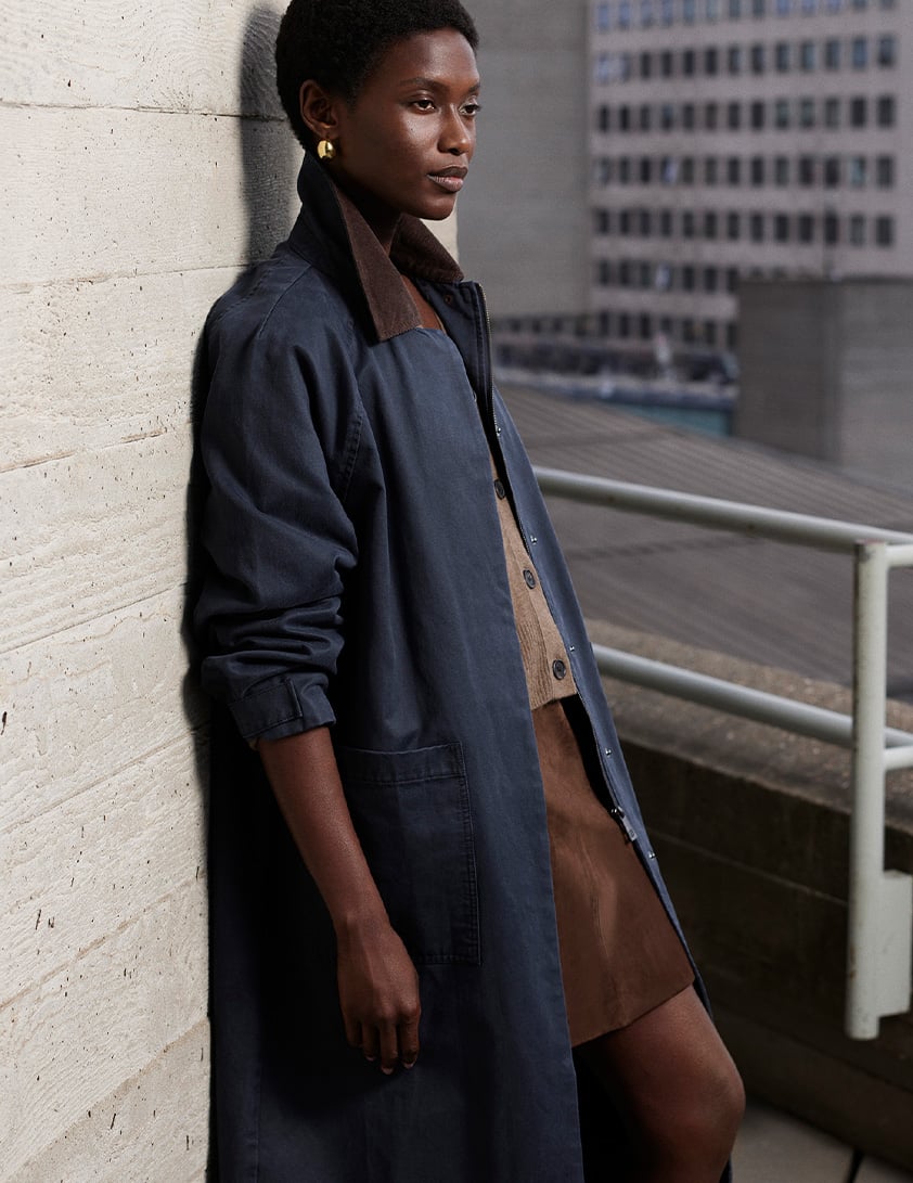 Woman wearing Whistles navy long coat with brown collar styled with brown suede skirt and gold earrings.