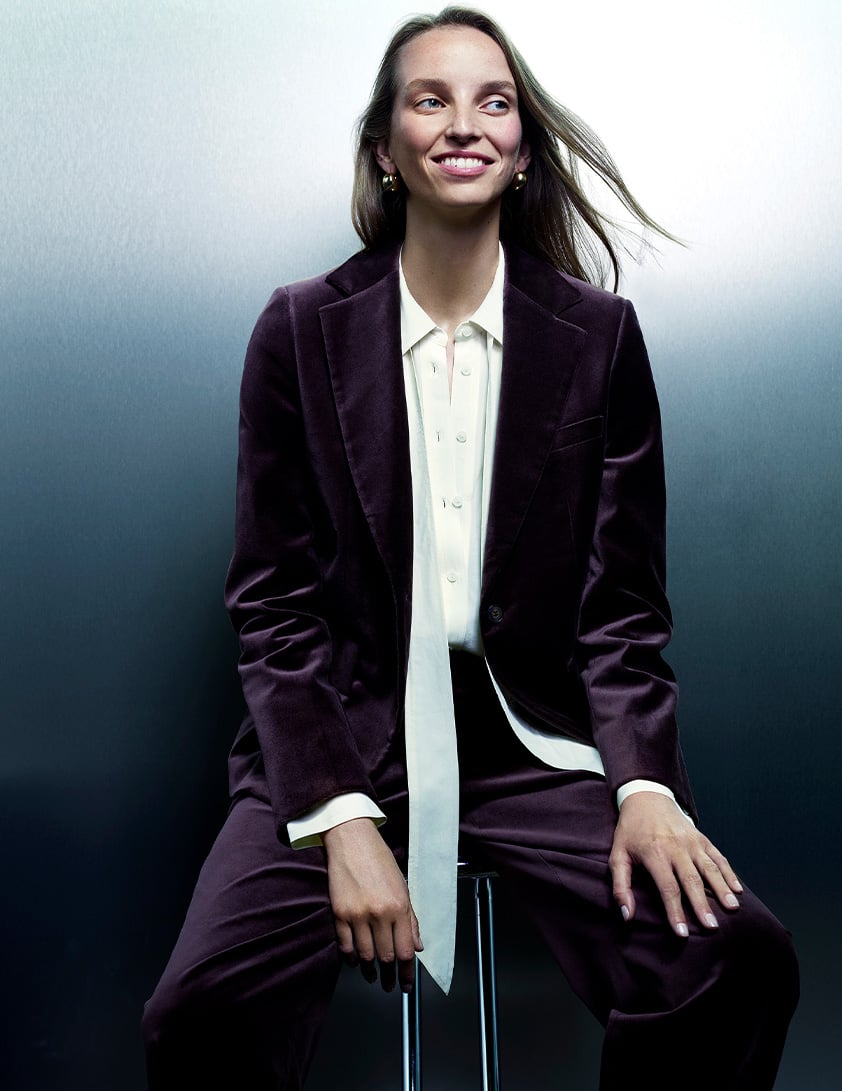 Woman wearing a Whistles purple velvet blazer with matching tailored pants, layered over a white button-down shirt
