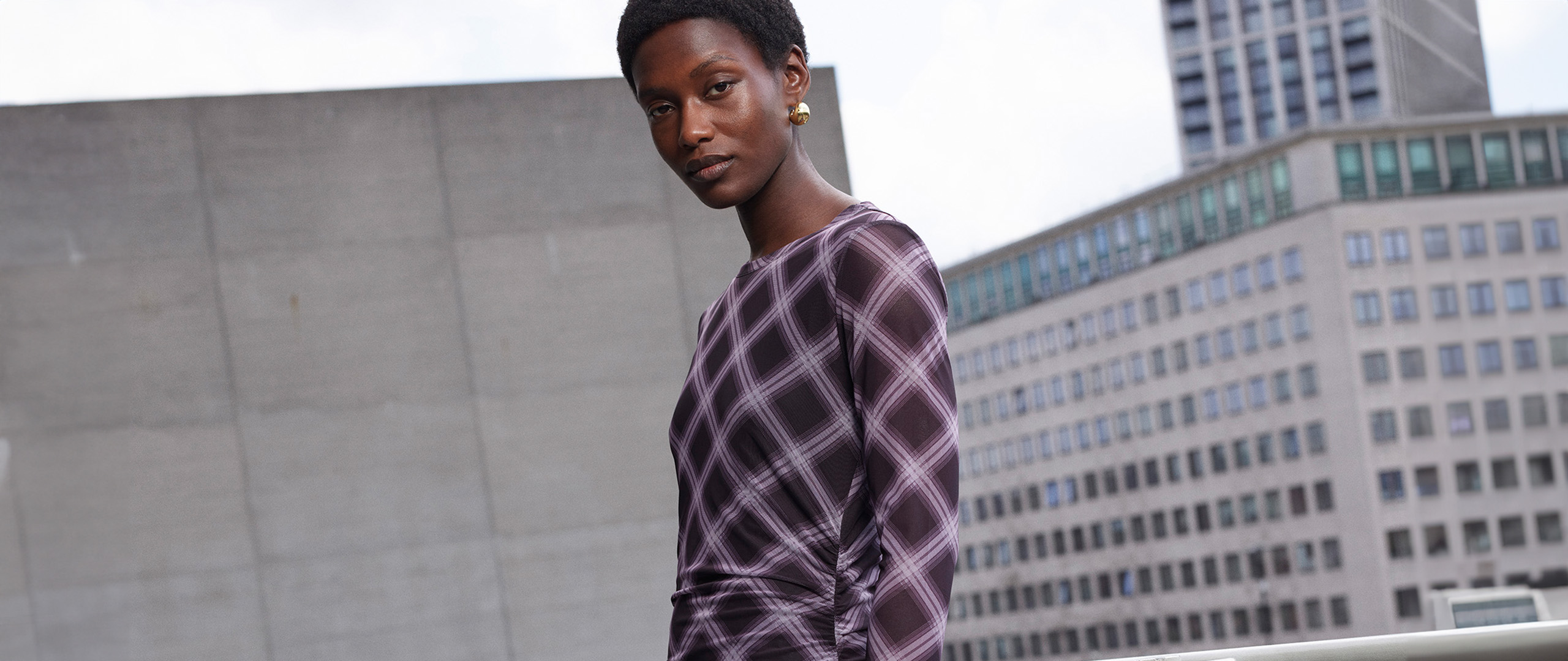 Woman wearing Whistles purple checked long sleeve maxi dress with gold earrings.