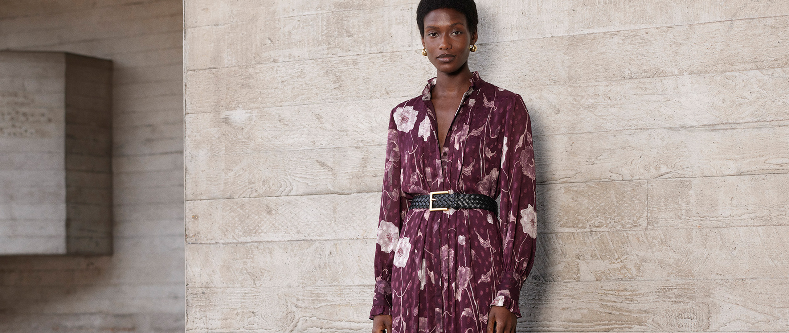 Woman wearing Whistles' purple floral midi dress with a V-neck and long sleeves, styled with a black woven belt and black suede boots