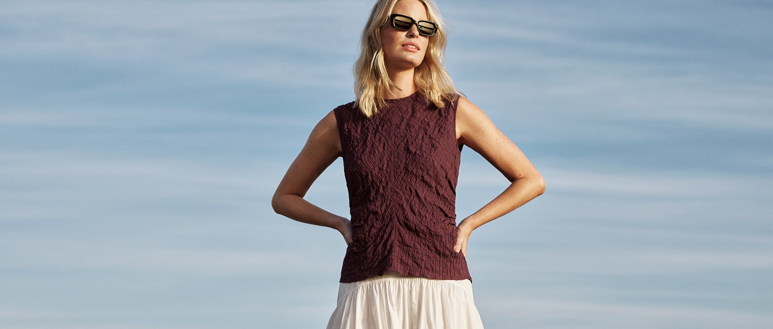Woman wearing a sleeveless burgundy textured top with cream skirt for Whistles 25% off everything labor day promotion