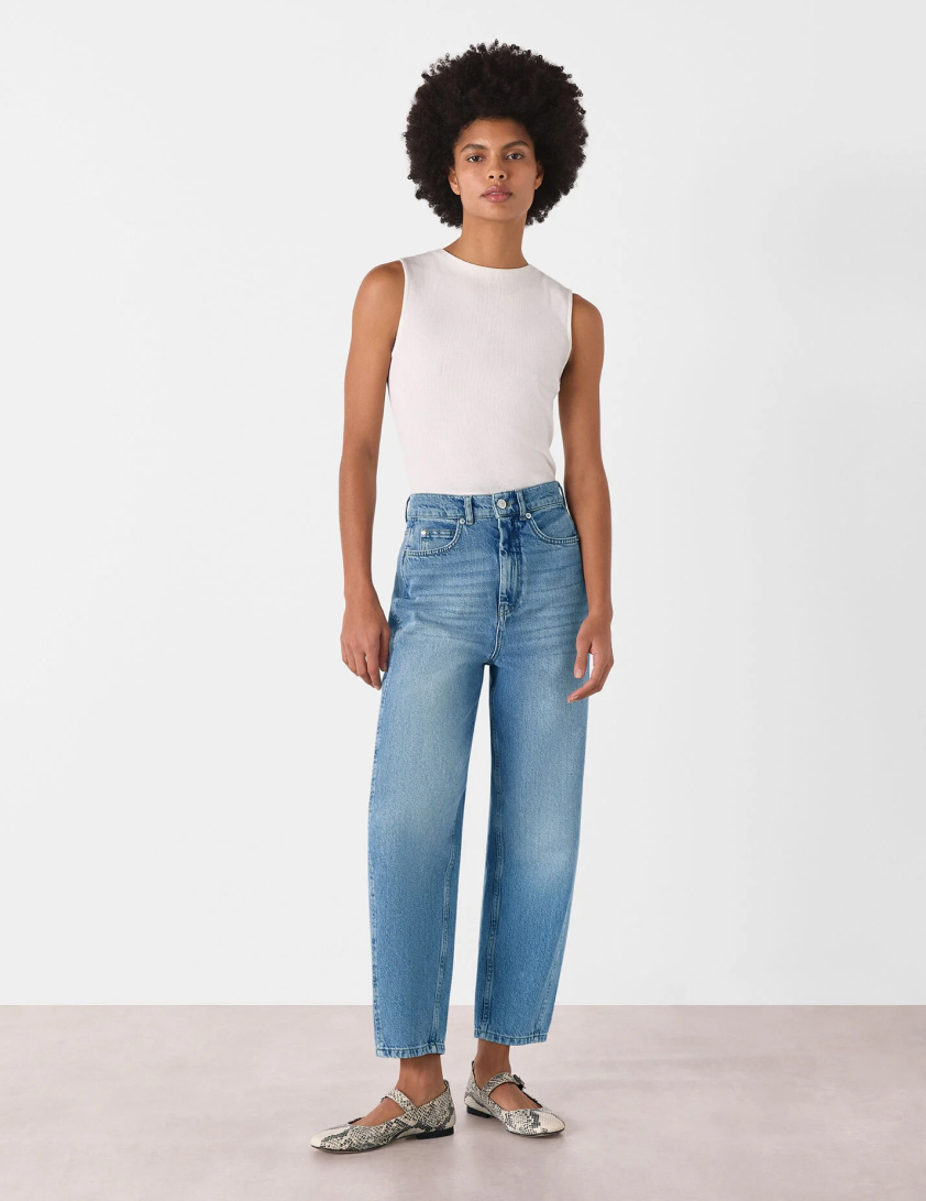Woman wearing a sleeveless white top with high waisted wide leg light blue jeans for Whistles 25% off everything labor day promotion