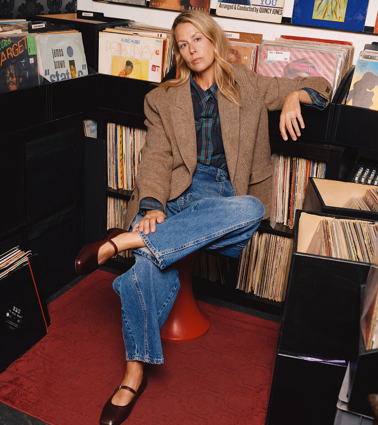Jody in a record shop wearing a brown herringbone double-breasted blazer and lantern jeans