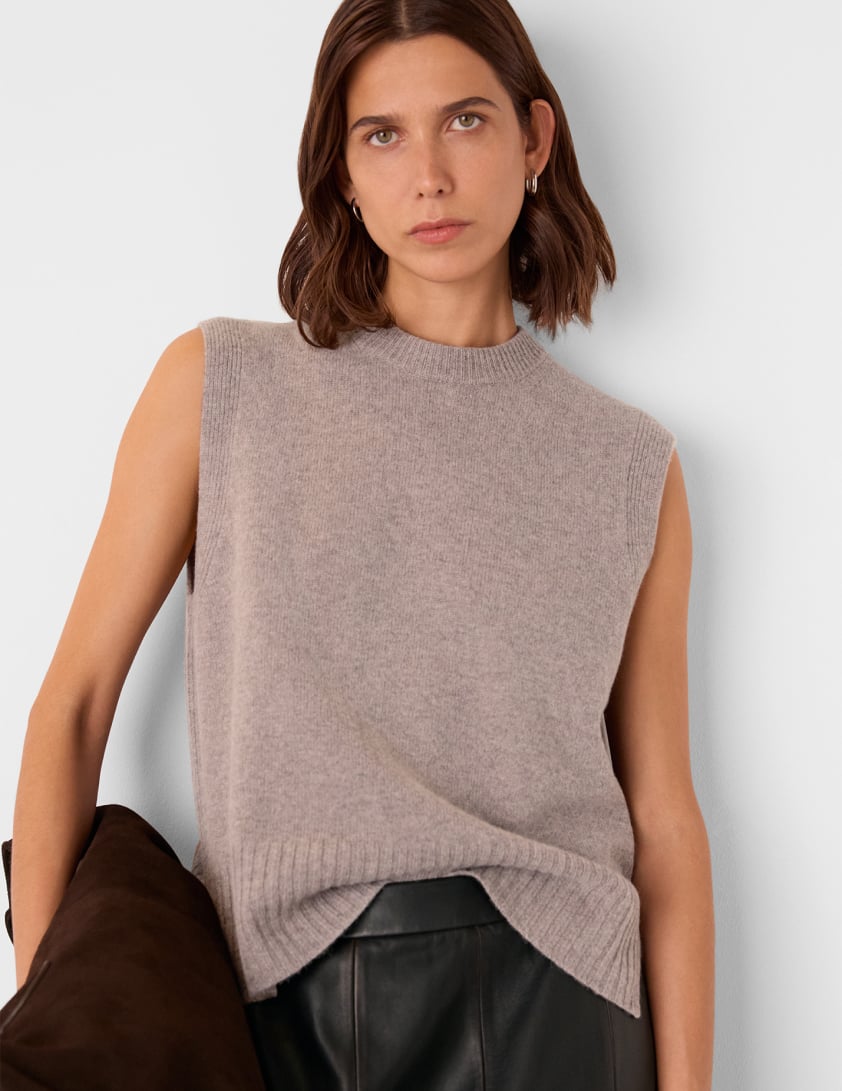 Model wearing Whistles sleeveless taupe knit top with black leather skirt, holding a chocolate suede bag